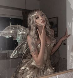 a woman dressed as a fairy standing in front of a mirror holding her hand up to her face