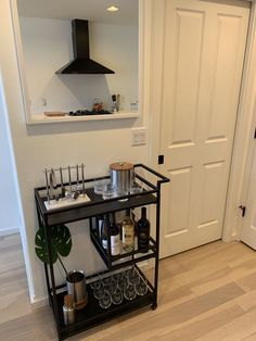 a black shelf with bottles and glasses on it in front of a white door next to a potted plant