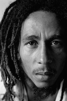 a black and white photo of a man with dreadlocks looking at the camera