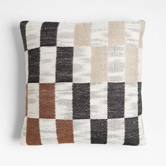 a black, white and brown pillow with squares on it's back side in front of a white wall