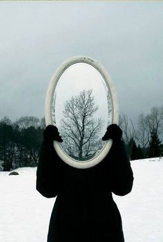 a person standing in the snow holding a frisbee up to their face with trees in the background