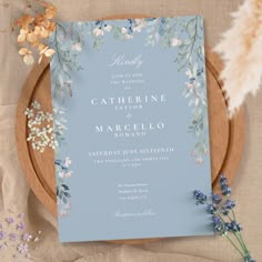 a blue and white wedding card on a wooden plate with dried flowers in the background