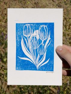 a hand holding up a blue and white card with flowers on it in the grass