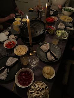 a group of people sitting around a table with food on it and candles in the middle