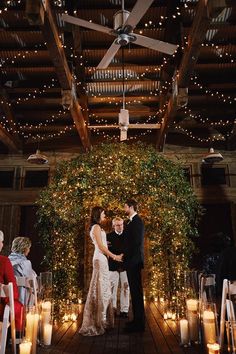 a bride and groom are standing in front of candles at their wedding ceremony, surrounded by greenery