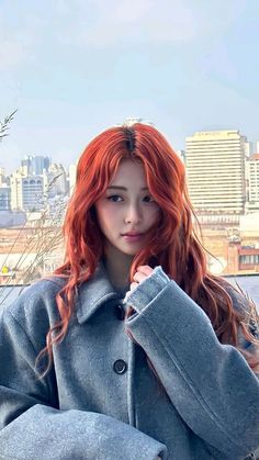 a woman with red hair is standing in front of a cityscape and looking at the camera