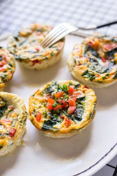 mini quiches with spinach, tomatoes and cheese on a white plate next to a fork