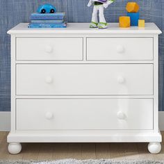 a child's bedroom with blue wallpaper and white dresser in the foreground