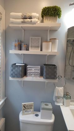 a white toilet sitting in a bathroom next to a sink under a shelf filled with towels