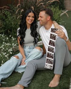 a man and woman sitting on the grass with their arms around each other, smiling