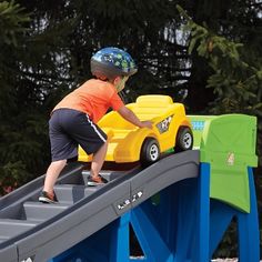 a young boy riding on the back of a yellow toy car over a green and blue ramp