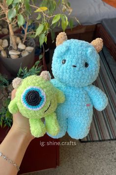 two crocheted stuffed animals sitting next to each other in front of a potted plant