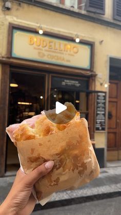 someone holding up a piece of food in front of a building