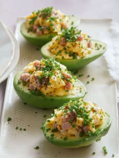 four stuffed green peppers with toppings on them sitting on a white plate next to a fork