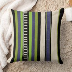 a green, blue and black striped pillow on a white rug next to a towel