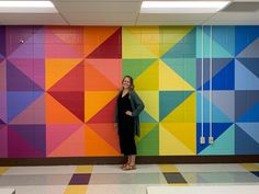 a woman standing in front of a colorful wall with geometric designs on it and smiling at the camera