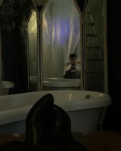 a man is taking a photo in the reflection of a bathtub with his feet propped up