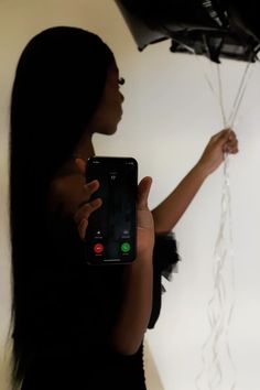 a woman holding up a cell phone in front of a wall with balloons attached to it