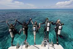 five people in scuba gear standing on a boat with their hands up and arms raised