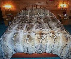 a large bed with fur on it in a room next to two lamps and a wooden headboard