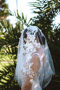 the back of a bride's veil with white flowers on it, in front of palm trees