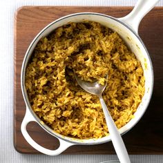 a large pot filled with rice on top of a wooden cutting board next to a spoon