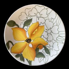 a yellow flower on a white plate with green leaves and flowers painted on the side