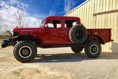 an old red truck parked in front of a building with large tires on it's flatbed