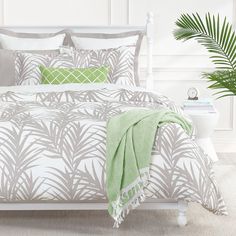 a bed with green and white pillows on top of it next to a potted plant