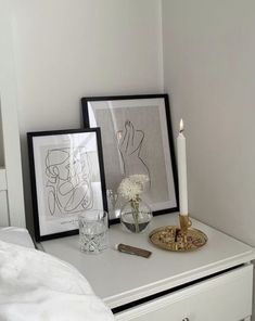 a white dresser topped with two pictures and a vase filled with flowers next to a lit candle