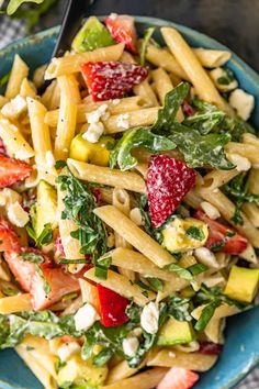 pasta salad with strawberries and spinach in a blue bowl on top of a table