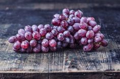 bunches of purple grapes sitting on top of a wooden table