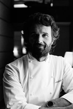 a black and white photo of a man in a chef's coat with his arms crossed