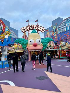 people standing around in front of an amusement park with clowns and rides on it