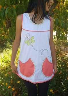 a woman standing in front of some trees wearing a white dress with pink and yellow flowers on it