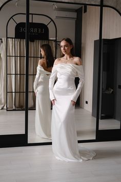 a woman standing in front of a mirror wearing a white dress and holding her hands on her hips