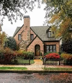 a brick house with trees and bushes in the front yard on a rainy fall day