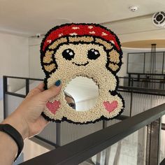 a person holding up a beaded stuffed animal in the shape of a smiling face