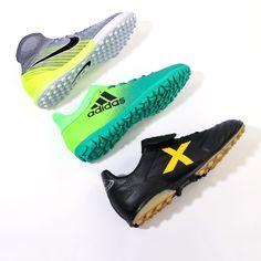 three pairs of soccer shoes on a white surface, one black and the other green