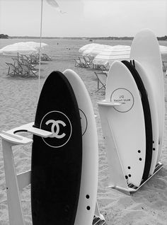 two surfboards sitting on top of a sandy beach next to chairs and umbrellas