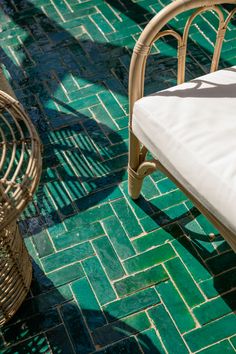 a wicker chair sitting on top of a green tile floor next to a white pillow