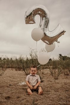 a little boy sitting on the ground with some balloons