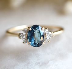 an oval blue and white diamond ring with three smaller diamonds on the side, set in yellow gold