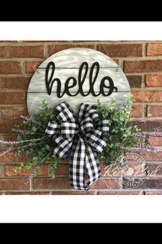 a wooden sign that says hello with a bow hanging on the side of a brick wall