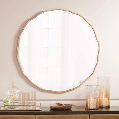 a round mirror sitting on top of a wooden dresser next to candles and vases