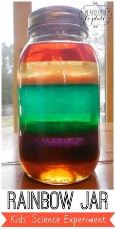 a jar filled with rainbow colored liquid sitting on top of a table next to a window