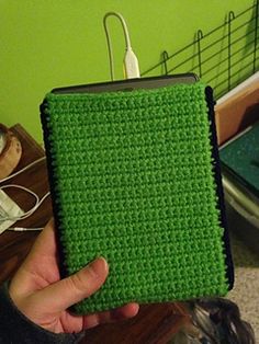 a person holding up a green crocheted case