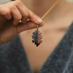 a woman is holding a necklace with leaves on it