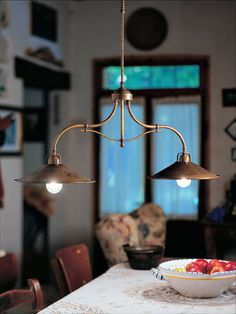 two lights hanging over a dining table in a room with chairs and a bowl of fruit on the table