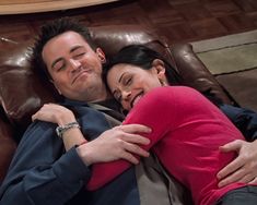 a man and woman laying on top of a brown leather couch smiling at the camera